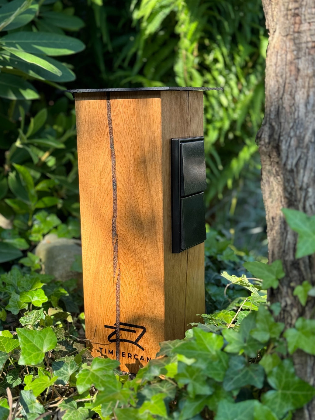 Timbercan Design-Steckdosensäule in der Black-Edition im Garten.
