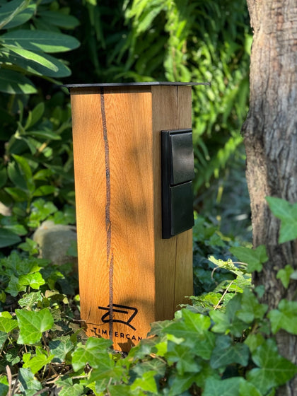 Timbercan Design-Steckdosensäule in der Black-Edition im Garten. 