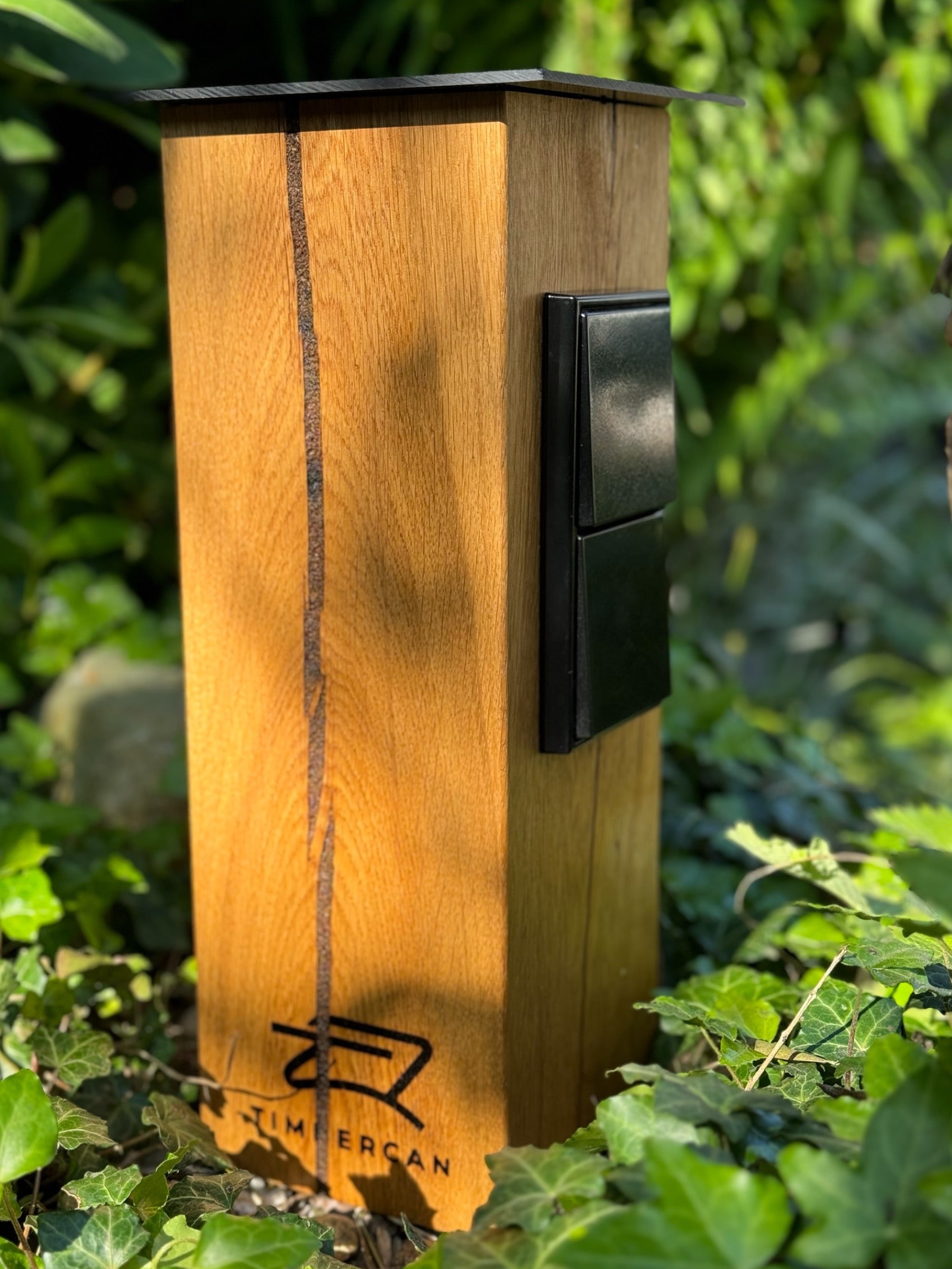 Steckdosensäule in der Black-Edition an einem sonnigen Tag im Hochbeet. 