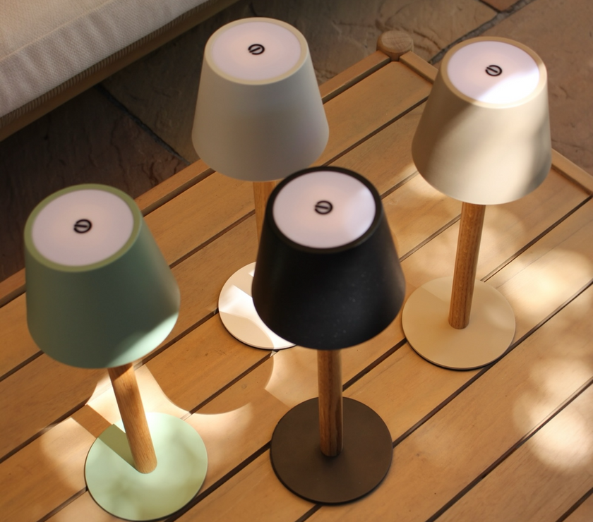 Vier TIMBERCAN Akku-Tischlampen aus Eichenholz in Schwarz, Grün, Beige und Weiß auf Terrassentisch – kabellose LED-Designleuchten für Indoor & Outdoor