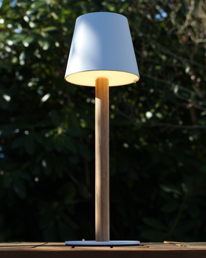 Beleuchtete weiße TIMBERCAN Akku-Tischlampe aus Eichenholz auf einem Terrassentisch im Garten – kabellose LED-Outdoor-Leuchte