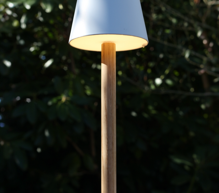 Beleuchtete weiße TIMBERCAN Akku-Tischlampe aus Eichenholz auf einem Terrassentisch im Garten – kabellose LED-Outdoor-Leuchte