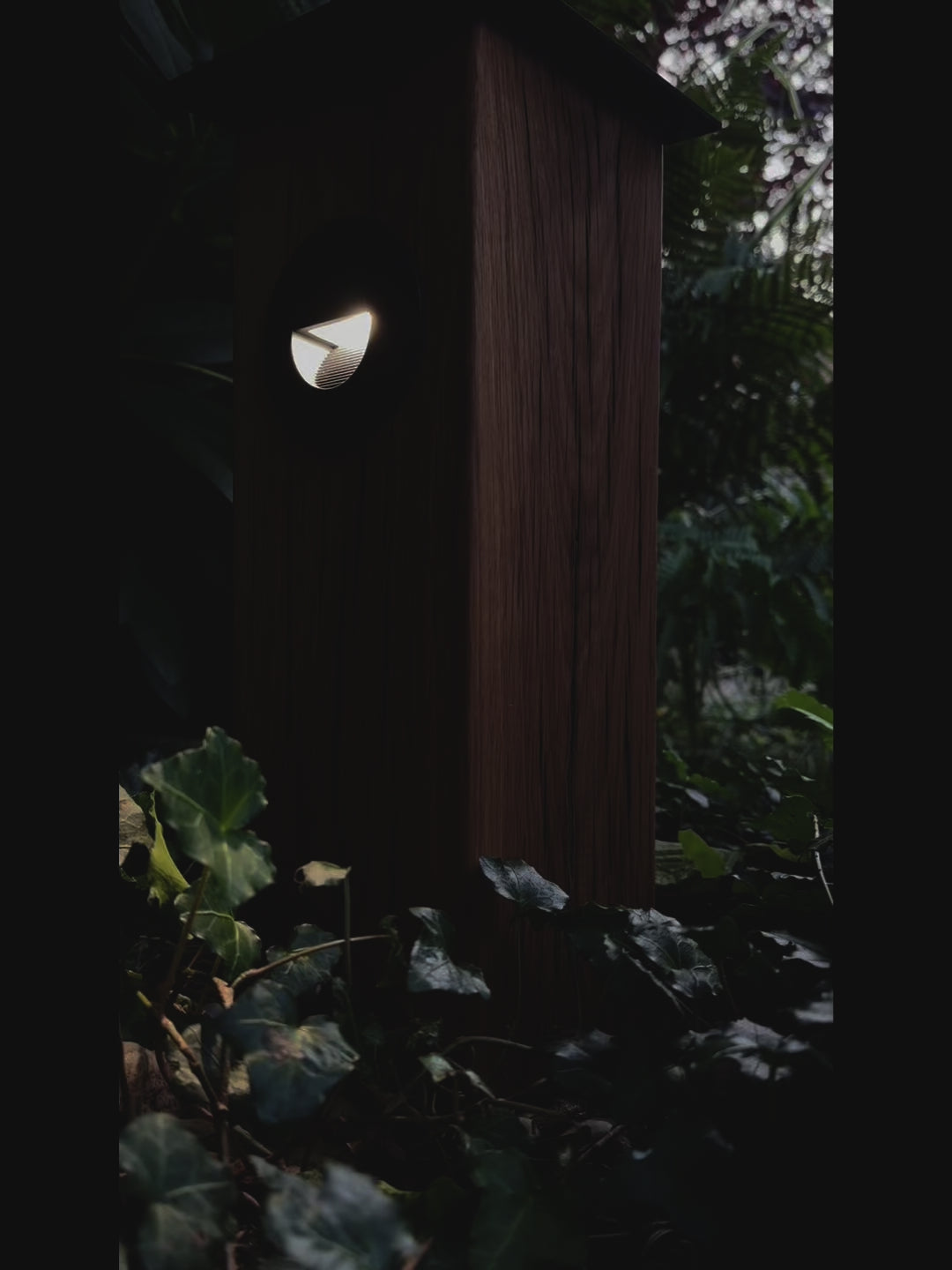 Timbercan Design-Wegleuchte mit eingeschalteter LED in der Dämmerung im Garten. 