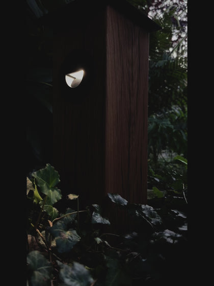 Timbercan Design-Wegleuchte mit eingeschalteter LED in der Dämmerung im Garten. 